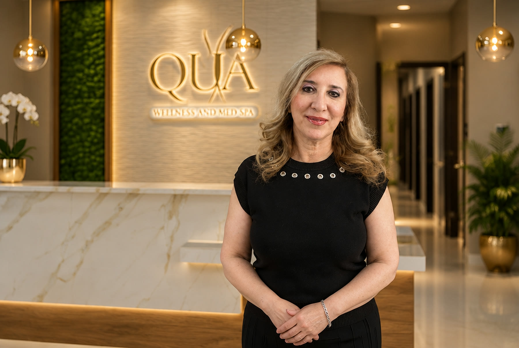 Dr. Maha Abboud at the Qua Wellness and Med Spa reception in Burr Ridge, in front of the gold Qua sign